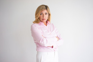 Closeup portrait of serious middle-aged attractive fair-haired woman looking at camera and standing...