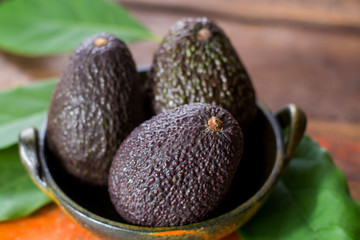 Raw ripe dark green avocados with leaves on wooden background