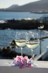 Two glasses with cold white wine served outside on terrace with pink tropical flowers, luxury resort with sea view, romantic vacation