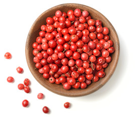dried pink peppercorns in the wooden plate, isolated on white, top view