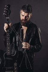 Bearded man, guitarist in black leather jacke with electric guitar. Hobby, music instrument, education, entertainment, concert and learning concept. Charismatic and stylish man holds guitar strings.