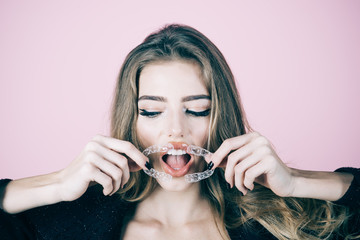 Teeth retainer. Sensative young woman holds transparent orthodontic device. Close up of plastic transparent retainer in hand of pretty young woman. Girl try to put orthodontic appliance in mouth.