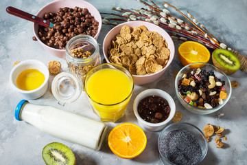 Healthy breakfast with bowl of cereal, orange juice, granola, milk, jam and fruits on concrete background.