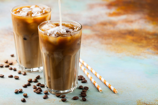 Ice Coffee In A Tall Glass With Cream Poured Over And Coffee Beans. Cold Summer Drink On A Blue Rusty Background With Copy Space