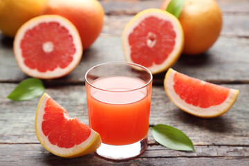 Ripe grapefruits and glass of juice on grey wooden table