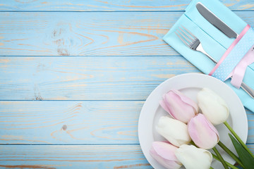 Kitchen cutlery with plate and tulip flowers on blue wooden table