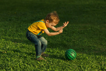 Cute positive kid, playing happily with ball on green meadow