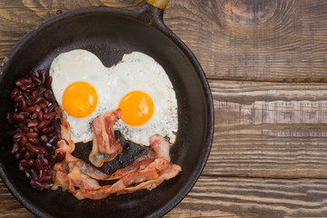 Bacon,Egg and bean. Salted egg and sprinkled with black pepper. English breakfast. Grilled bacon, two eggs and beans in pan on wooden table