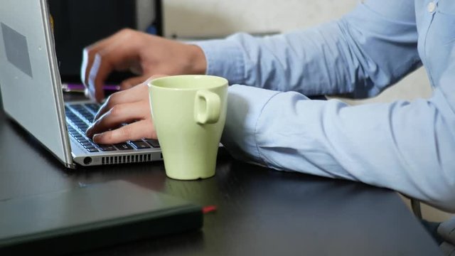 Young man sipping tea on laptop while working in office. close-up, 4k
