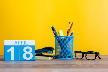 April 18th. Day 18 of month, calendar on business office table, workplace with yellow background....