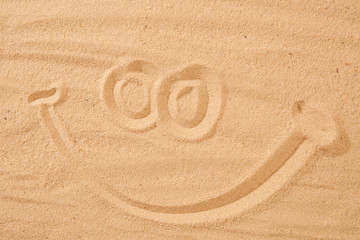 Handwrited face on the sand at the beach. Symbol smile on beach background.
