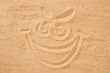 Handwrited face on the sand at the beach. Symbol smile on beach background.