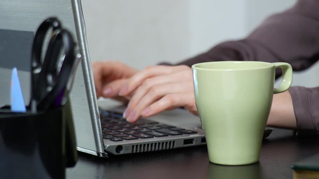 Young woman sipping tea on laptop while working in office. close-up, 4k