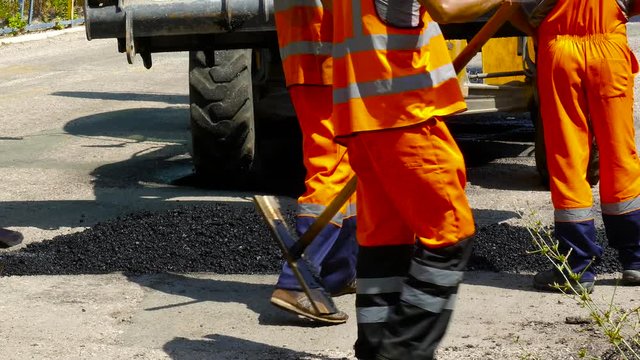 Workers are dragged with fresh asphalt from the car into the pit on the road