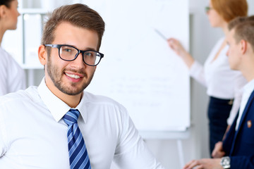 Business people at meeting in office. Focus at cheerful smiling bearded man wearing glasses. Conference, corporate training or brainstorming of people group. Success and negotiation concept