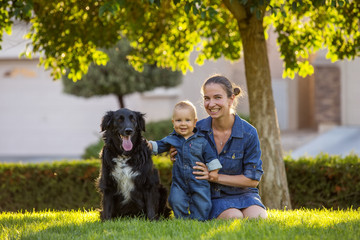 A mother with baby son and black dog in green neighborhood