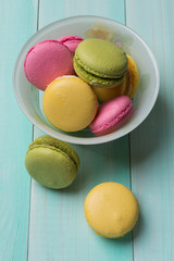 multicolored makroons in a plate on green wooden boards, macaros lie side by side on boards