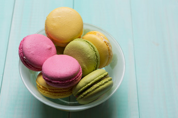 multicolored macarosa in a plate on green wooden boards
