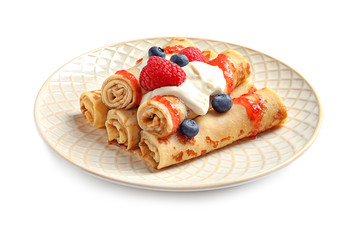 Thin pancakes with syrup, cream and berries on plate against white background