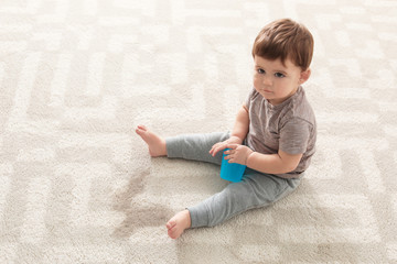 Naklejka premium Baby sitting on carpet with empty glass