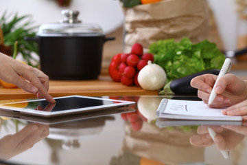 Closeup of human hands cooking in kitchen. Women discuss a menu using tablet computer. Copy space area at touch pad. Healthy meal, vegetarian food and lifestyle concepts