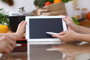 Closeup of human hands cooking in kitchen. Women discuss a menu using tablet computer. Copy space area at touch pad. Healthy meal, vegetarian food and lifestyle concepts