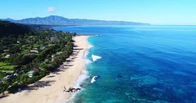 Aerial view flying over tropical white sand beach and clear blue water ocean on the North Shore of Hawaii on sunny day