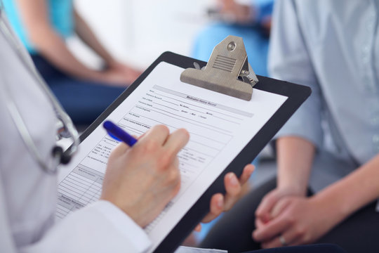 Close Up of a female doctor filling  out application form while talking to patient. Medicine and health care concept