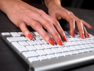 Red nail woman hand typing on wireless pc keyboard