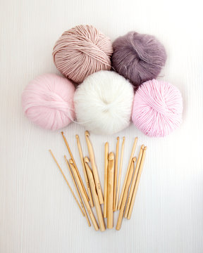 Wooden crochet hooks on white wood background with balls of yarn pastel colors. Top view. Hobby and handmade concept.