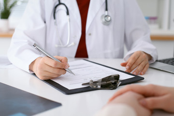 Close up of a female doctor filling up  an application form while consulting patient