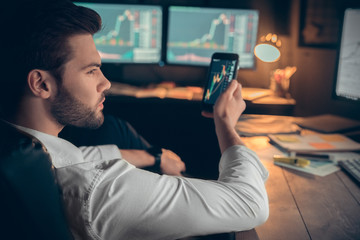 Young male trader at office work concept sitting holding smartphone