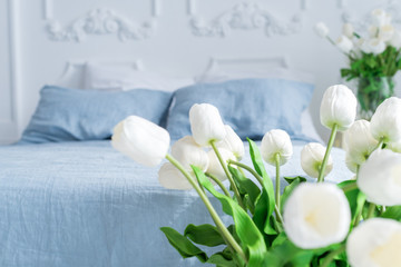 Delicate interior of a bedroom in blue tones with baskets and vases with tulips
