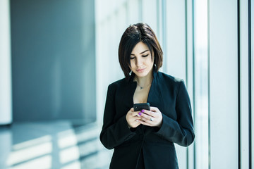 Obraz premium Portrait of a young business woman typing phone against panoramic windows