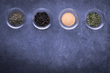 Row of ingredient dishes with Italian spices on a slate background and space for text on bottom