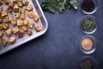 Flay lay of croutons on a baking sheet, beside spice dishes and space for text on bottom