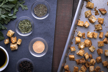 Top down view on ingredient dishes of spices on slate, beside a sheet pan of croutons