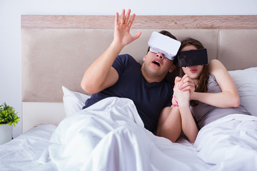 Wife and husband with virtual reality goggles in the bed