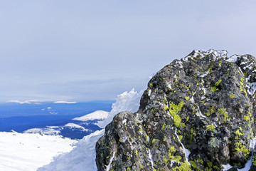 covered with lichen, weathered boulder in the snowy highlands against the background of a distant mountain landscape