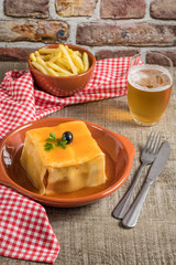 Traditional Portuguese snack food. Francesinha sandwich of bread, cheese, pork, ham, sausages, with tomato, beer, sauce and french fries. With a glass of beer and potatoes.