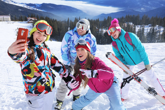 Happy friends taking selfie on ski piste at snowy resort. Winter vacation