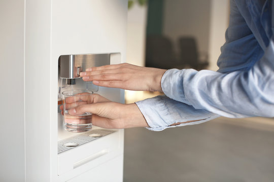 Woman filling glass from water cooler, closeup