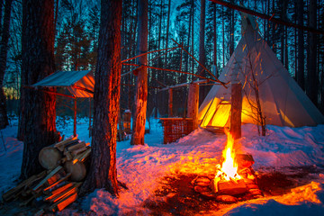 Tipi in the snow-covered forest. Indian parking. The bonfire burns at the entrance to the Wigwam....