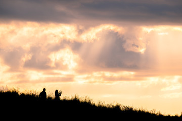 Naklejka na ściany i meble Silhouette scene of a couple enjoy with their drone at sunset on the top of Mt. Eden, Auckland, New Zealand.