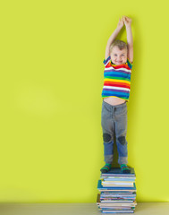 A joyful smiling child is standing on a stacked of children's books. Green background.
