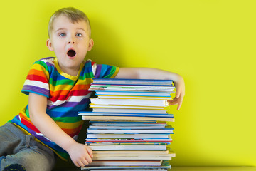 The child holds a large stacked of children's books in his hands. Green background.