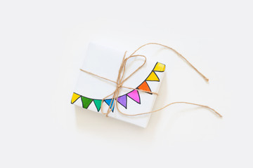 White gift box. Drawing of a colored garland, flags. White background. Confetti.