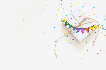 White gift box. Drawing of a colored garland, flags. White background. Confetti.