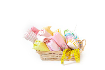 Colored cotton sewing fabrics lie in a wicker basket. Needle, centimeter and scissors. Isolate.