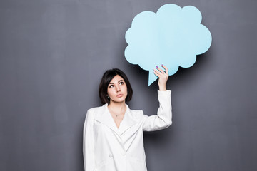 Cheerful attractive young business woman standing and holding blank speech bubble over grey background
